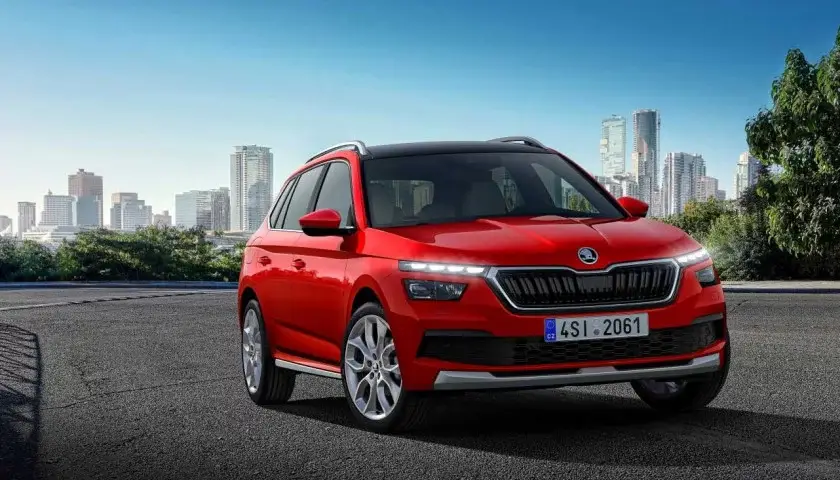 SUV Skoda rouge garé sur une route avec des gratte-ciel en arrière-plan et des arbres sur le côté droit.