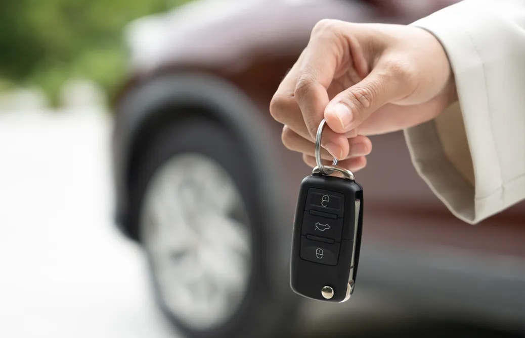 Une main tenant une clé de voiture noire, avec un véhicule flou en arrière-plan.