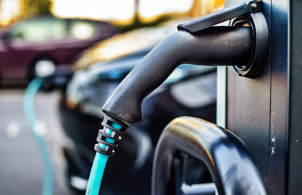 Une voiture électrique noire est branchée à une borne de recharge avec un câble bleu, en arrière-plan flou.