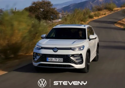 SUV Volkswagen Tayron blanc roulant sur une route de campagne, entouré de végétation et de collines en arrière-plan.