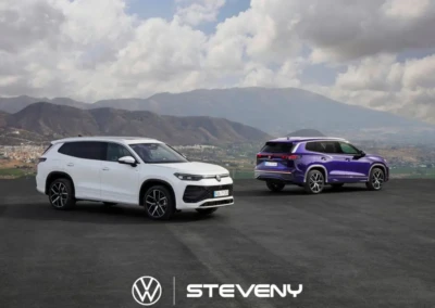 Deux SUV Volkswagen Tayron, l'un blanc et l'autre violet, stationnés sur une route avec des montagnes en arrière-plan.