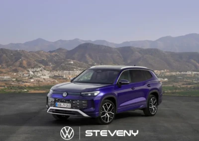 SUV Volkswagen Tayron bleu stationné sur une route, avec des montagnes en arrière-plan sous un ciel clair.