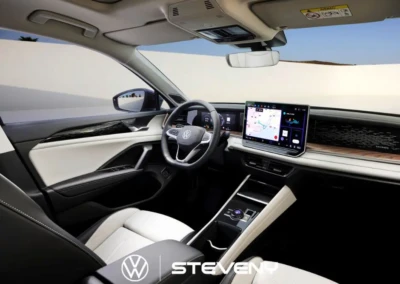 Intérieur d'un Volkswagen Tayron avec tableau de bord numérique et volant, sièges en cuir noir et blanc, écran central affichant une carte.