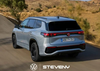 SUV Volkswagen Tayron argenté à sept places sur une route sinueuse, entouré de paysages désertiques et de collines.