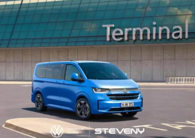 Volkswagen Transporter T7 bleu stationné devant un bâtiment avec une façade vitrée indiquant "Terminal".