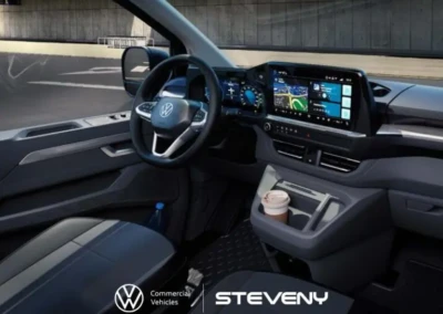 Intérieur du Volkswagen Transporter T7 avec tableau de bord numérique, volant multifonction et porte-gobelet contenant un café.
