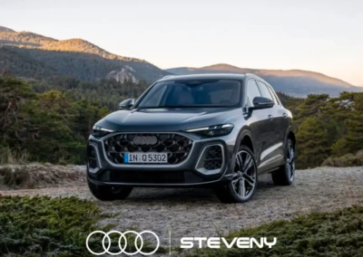 SUV Audi Q5 gris stationné sur un chemin de gravier, entouré de végétation et de montagnes en arrière-plan, logo Steveny visible.