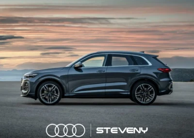 SUV Audi Q5 gris foncé stationné sur une route, avec un ciel de coucher de soleil en arrière-plan. Logo Steveny visible.