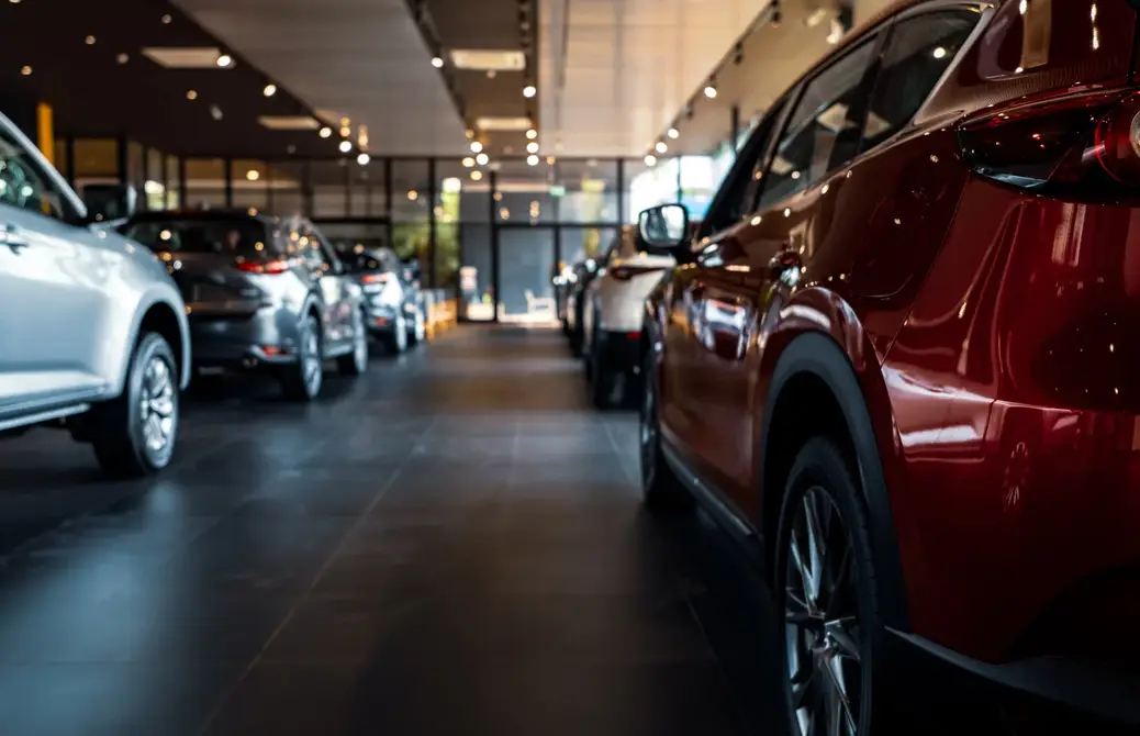 Voitures exposées dans une concession automobile moderne, avec un SUV rouge au premier plan et des modèles argentés alignés.